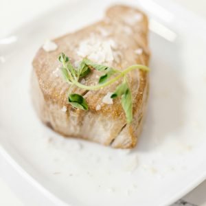 A delicious gourmet tuna steak garnished with greens, presented elegantly on a white plate.