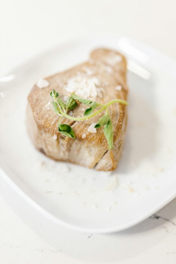 A delicious gourmet tuna steak garnished with greens, presented elegantly on a white plate.