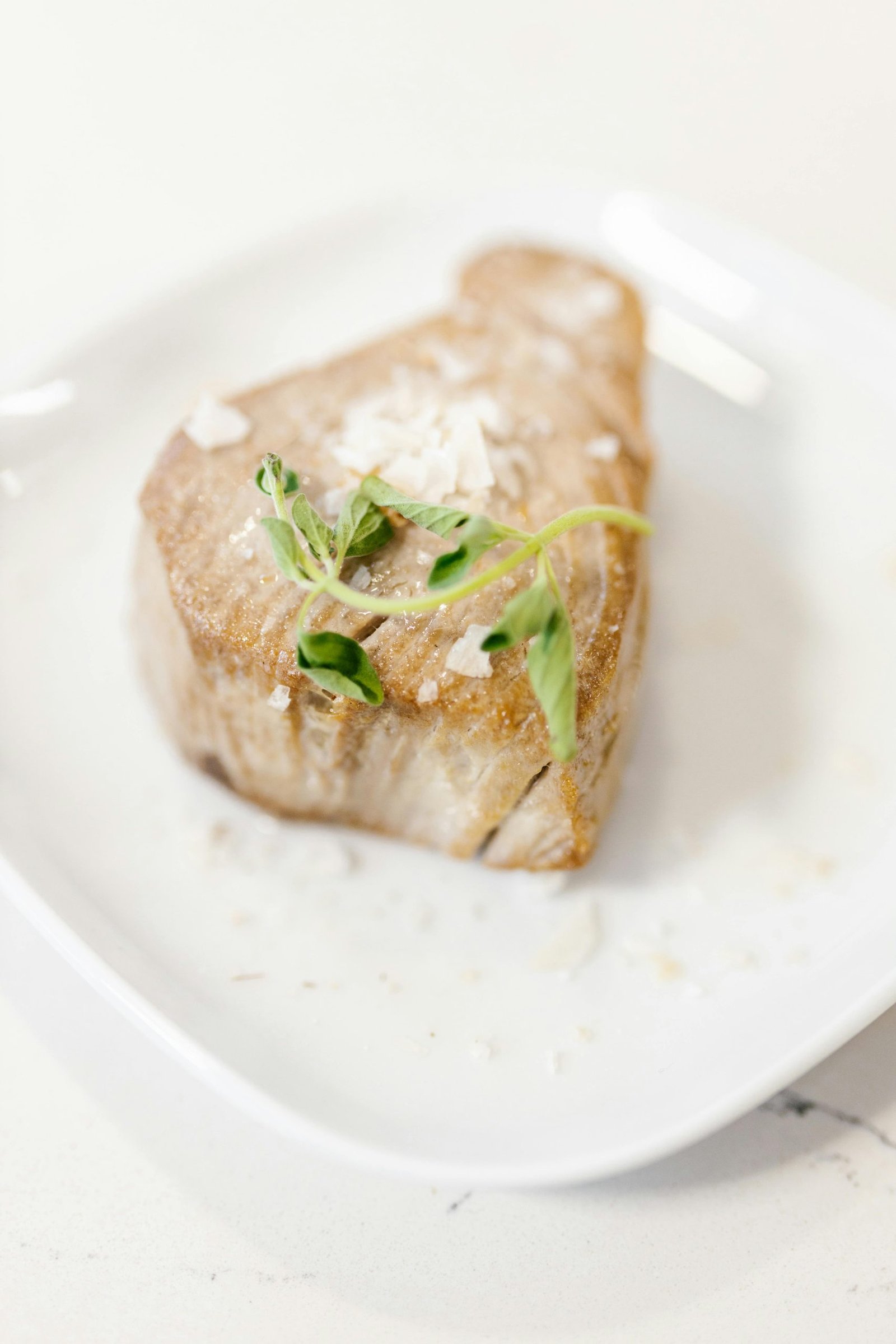 A delicious gourmet tuna steak garnished with greens, presented elegantly on a white plate.