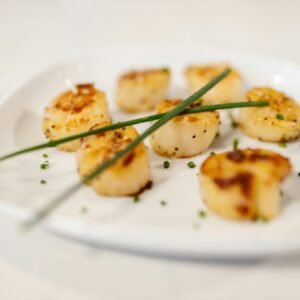 Delicious grilled scallops garnished with fresh chives on a white plate.