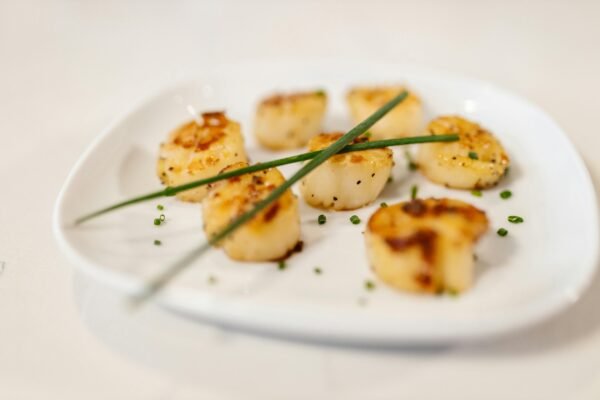 Delicious grilled scallops garnished with fresh chives on a white plate.