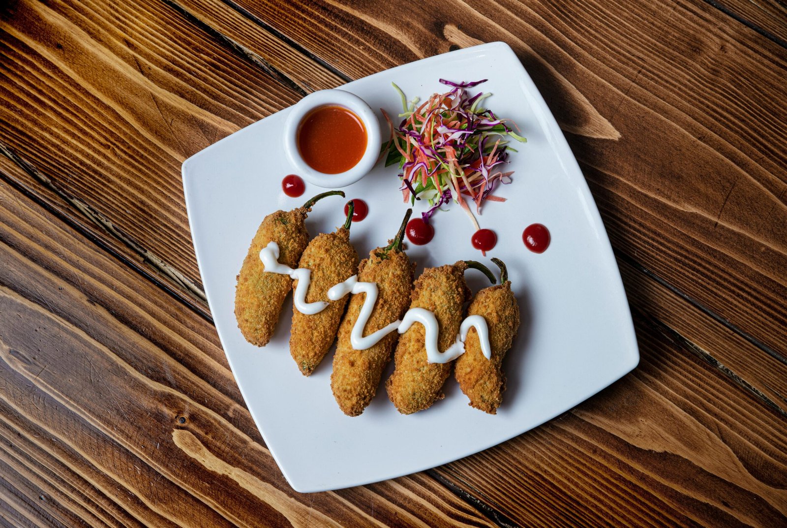 Delicious deep-fried jalapeño poppers with creamy dip and colorful salad on a white plate.