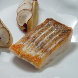 Delicious grilled fish fillet with artful slices of root vegetables on an elegant plate.