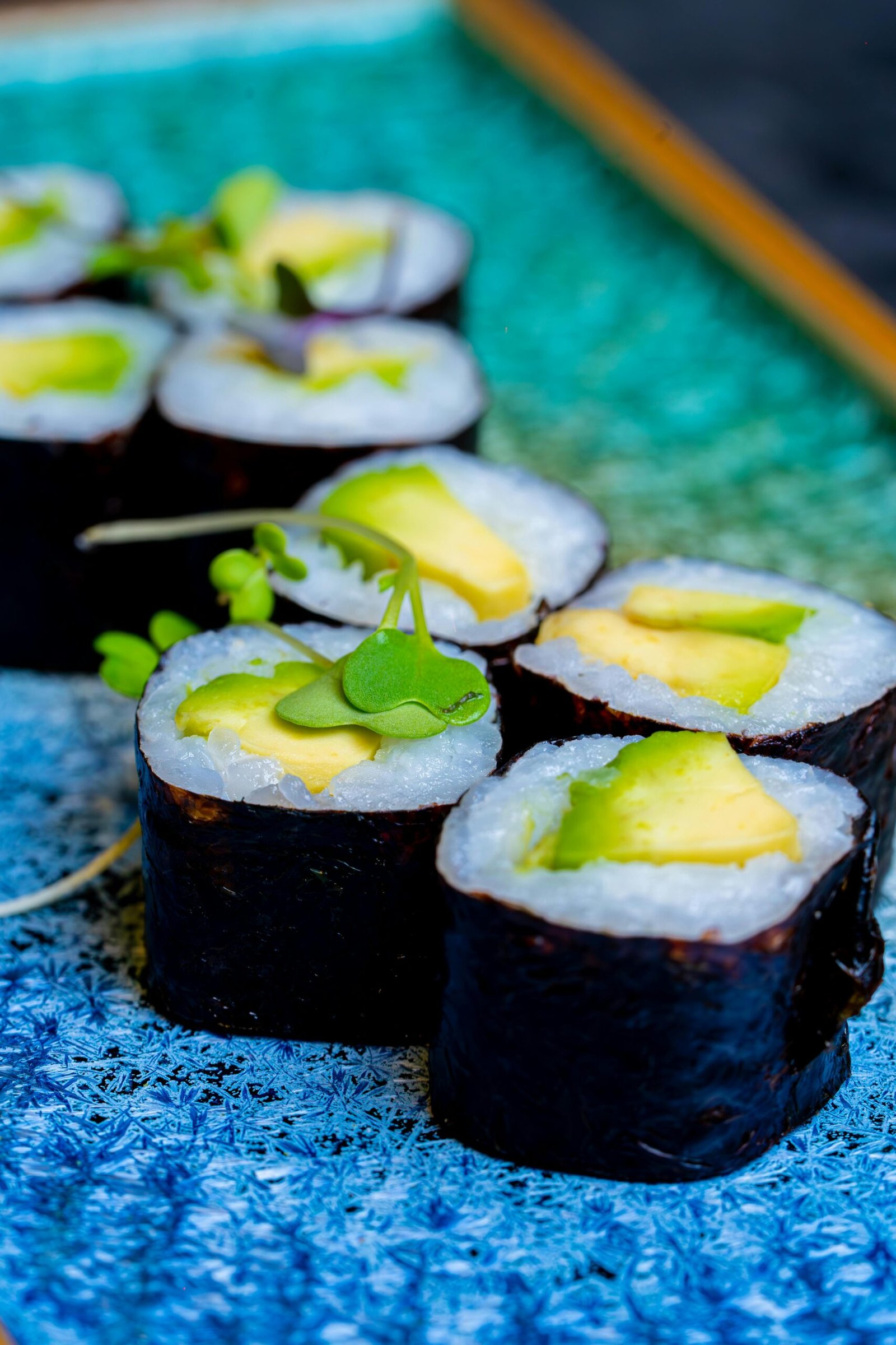 Vibrant vegetarian sushi rolls with avocado on a decorative blue plate. Perfect for healthy food themes.