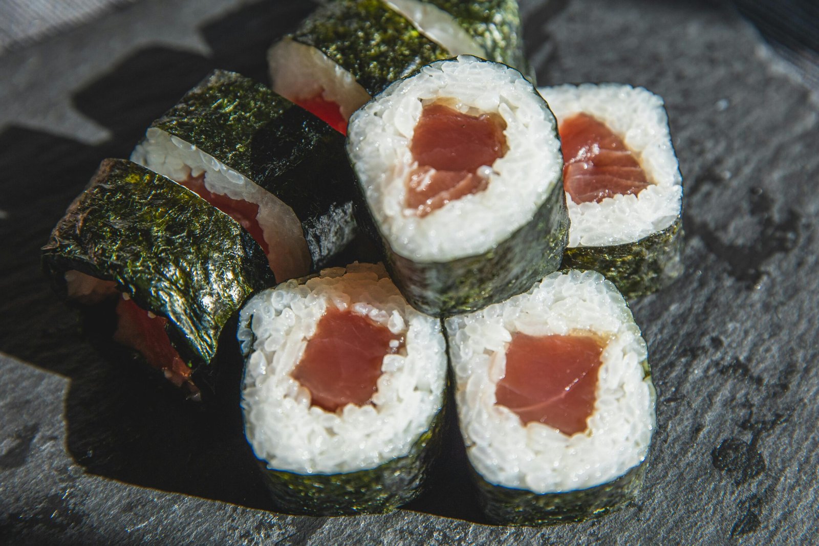 High-angle view of delectable tuna sushi rolls with nori wrap served on a slate plate.